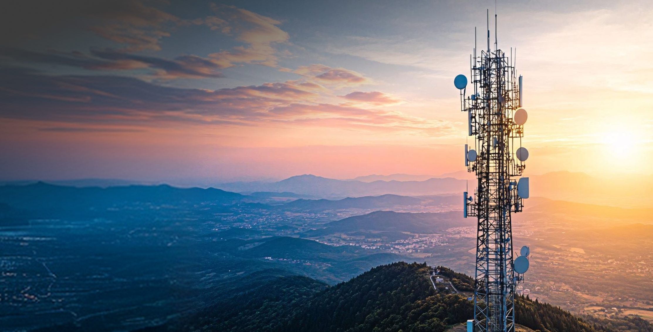 A telecommunications mast on a hilltop above a valley at sunrise